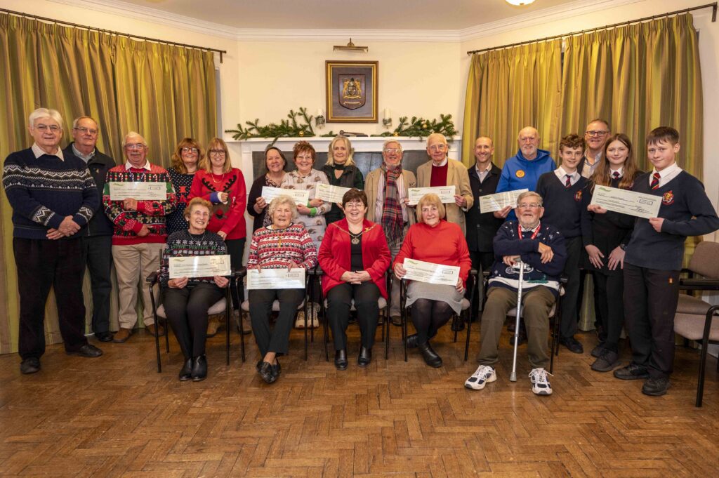 A group of people posed indoors, some standing some seated, holding large ceremonial checks at a grant presentation event.
