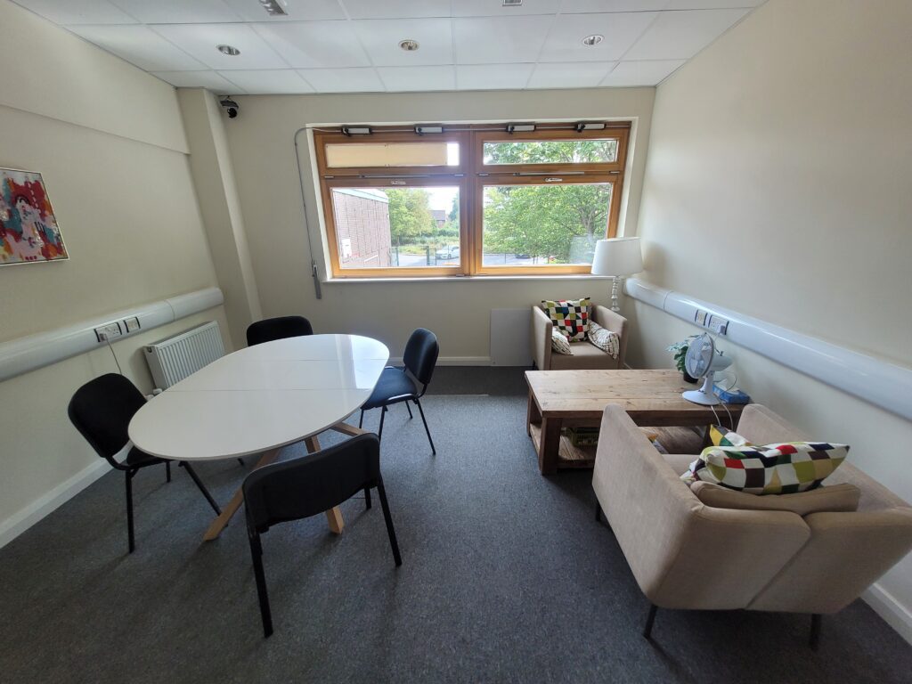 A small room with a round table and four chairs plus two arm chairs and a coffee table